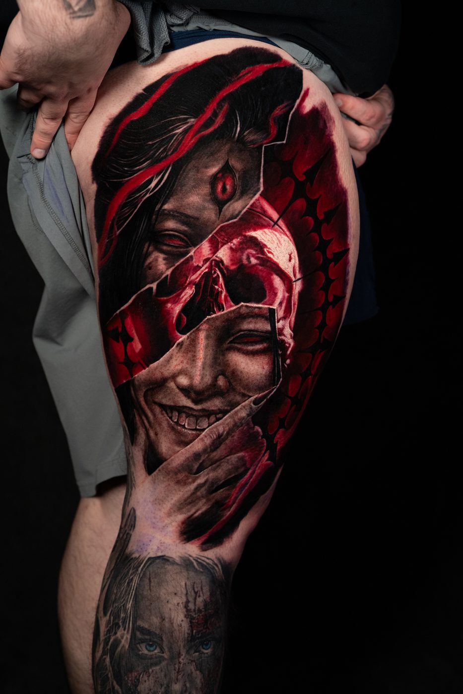 Red and black split-portrait realism thigh tattoo