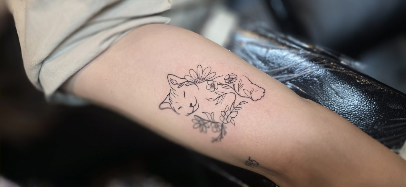 Fine-line sleeping cat and flowers tattoo