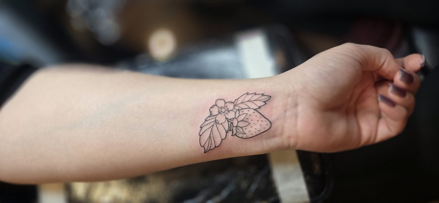 Fine-line strawberry and blossom wrist tattoo